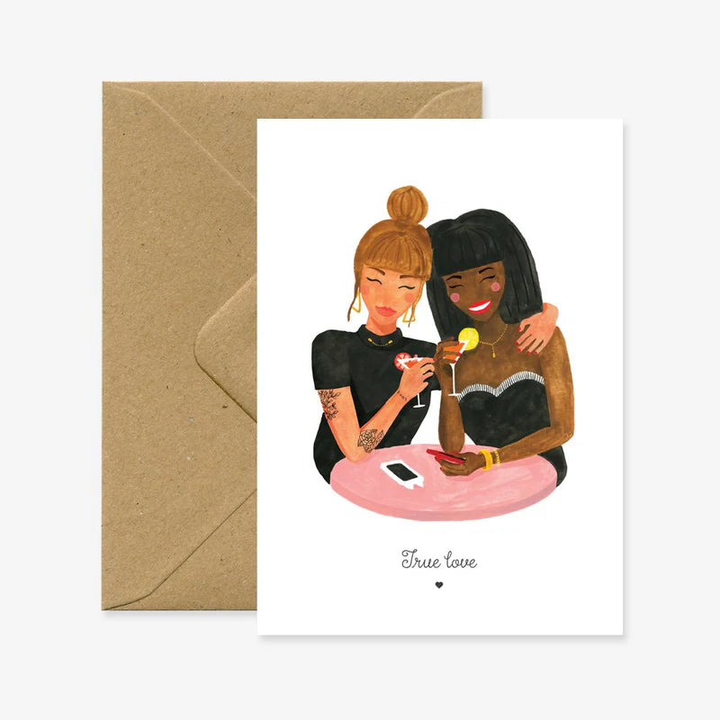 Zwei Frauen in schwarzer Kleidung sitzen an einem runden Tisch mit einem Smartphone, halten Cocktails und umarmen sich. Darunter steht 'True love'.