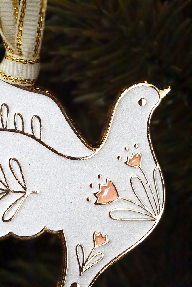 Weißer Taubenanhänger mit goldfarbenen Verzierungen hängt an einem Tannenzweig.