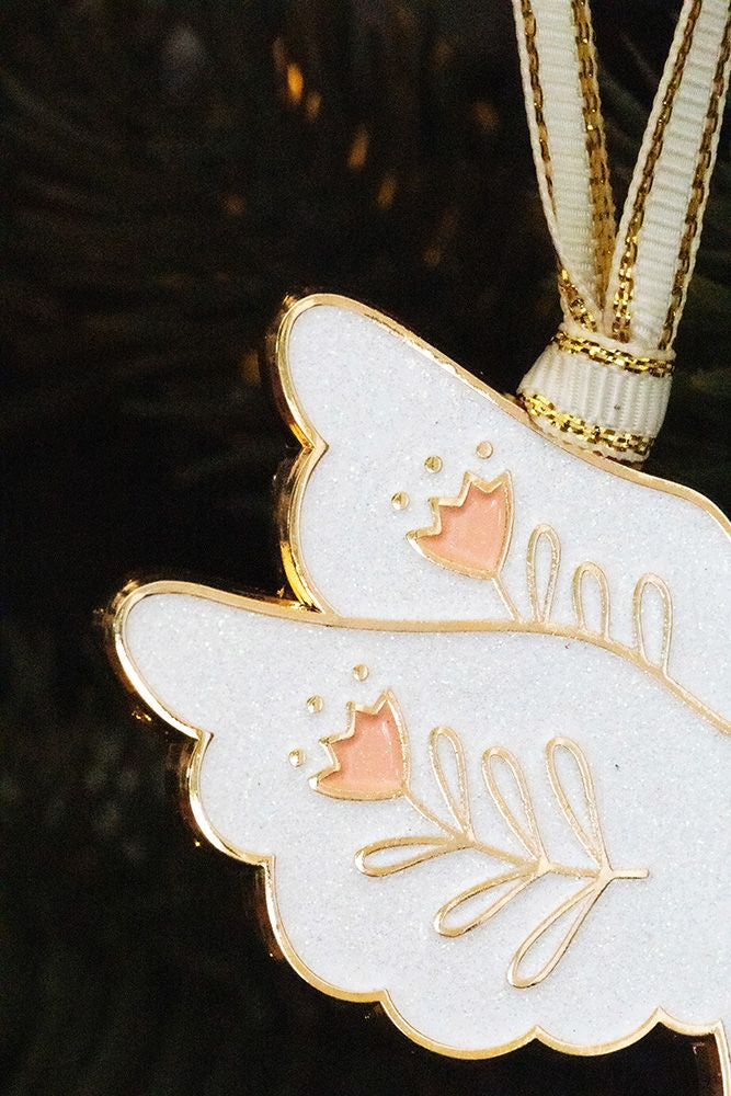 Weißer Taubenanhänger mit goldfarbenen Verzierungen hängt an einem Tannenzweig.