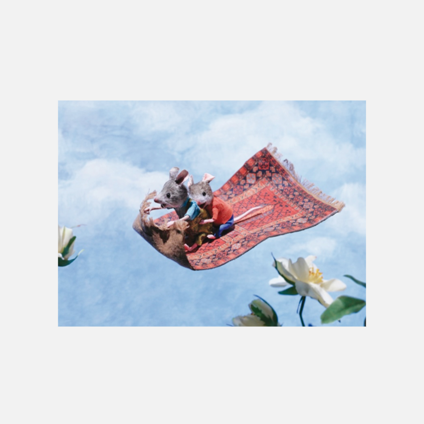 Zwei Mäusefiguren sitzen auf einem fliegenden Teppich über Blumen vor blauem Himmel