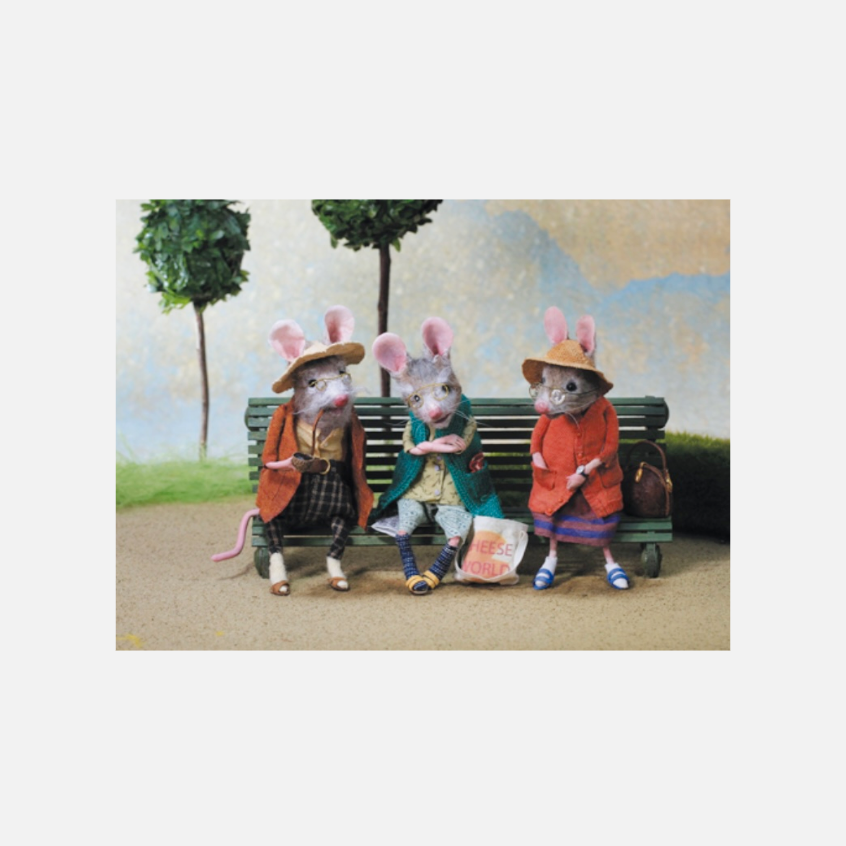 Drei anthropomorphe Mäuse mit Kleidung und Hüten sitzen auf einer Parkbank, zwei tragen orangefarbene Mäntel, eine einen grünen Mantel, im Hintergrund zwei Bäume