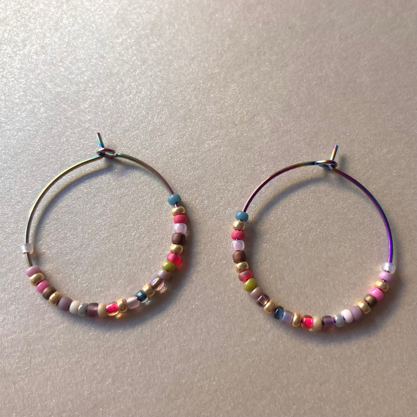 Zwei bunte Creolen-Ohrringe mit kleinen, mehrfarbigen Perlen.