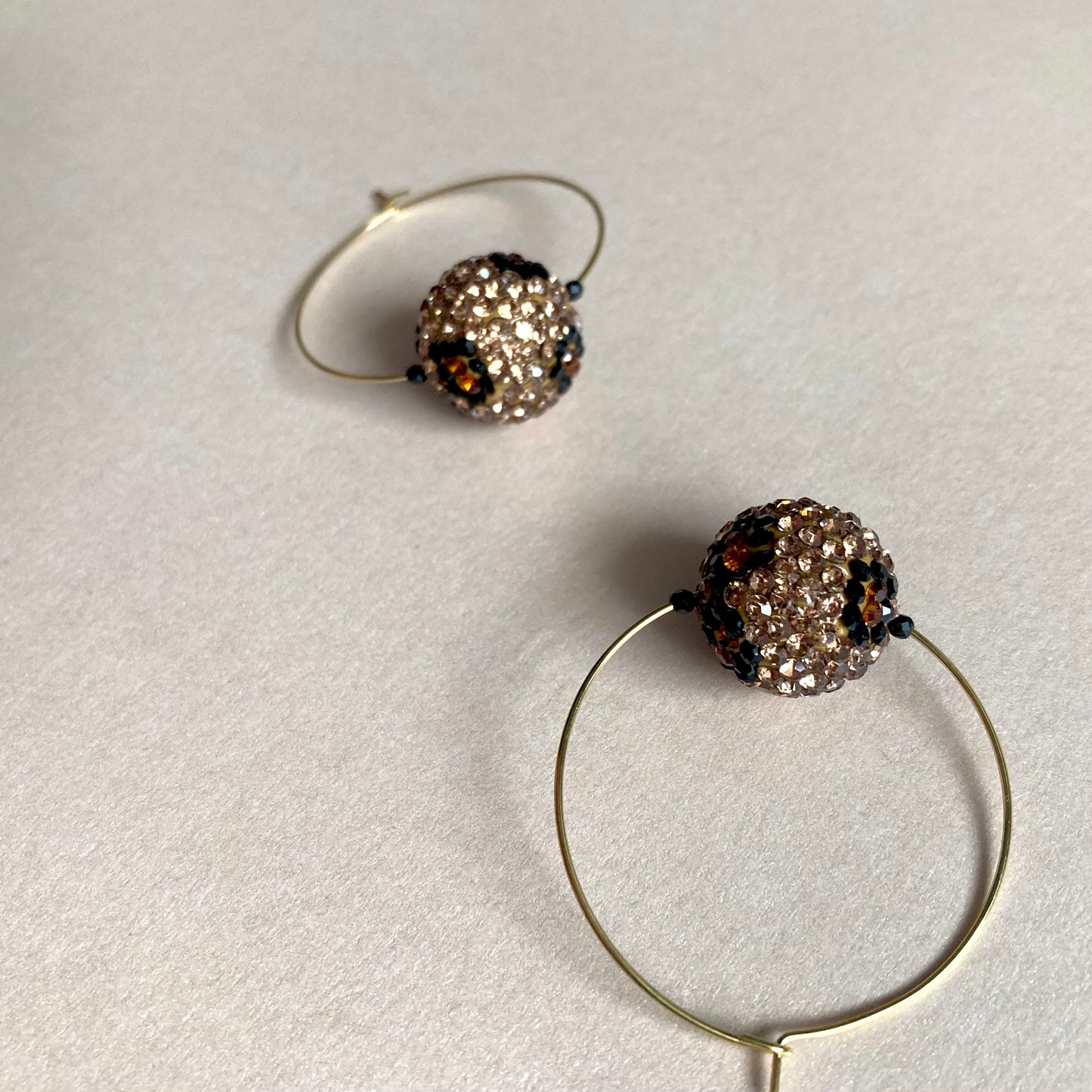 Zwei goldfarbene Creolen mit kugelförmigen Anhängern im Leopardendesign, die mit kleinen, glitzernden Strasssteinen besetzt sind