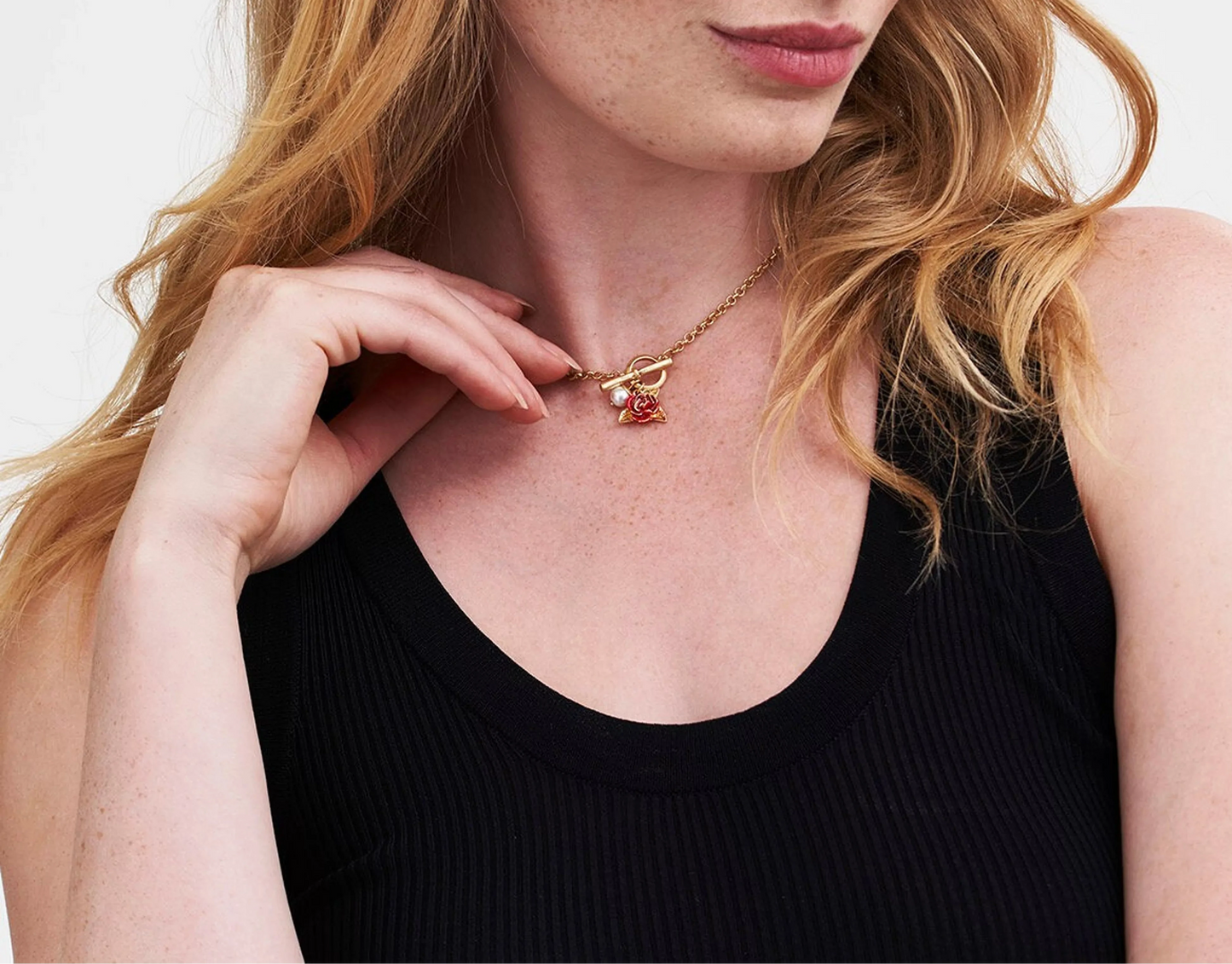 Elegante goldfarbene Halskette mit T-Steg-Knebelverschluss und dekorativem Anhänger. Der Anhänger besteht aus einem zarten roten Rosenanhänger mit goldenen Blättern und einer glänzenden weißen Perle, die für eine romantische und feminine Ästhetik sorgt.