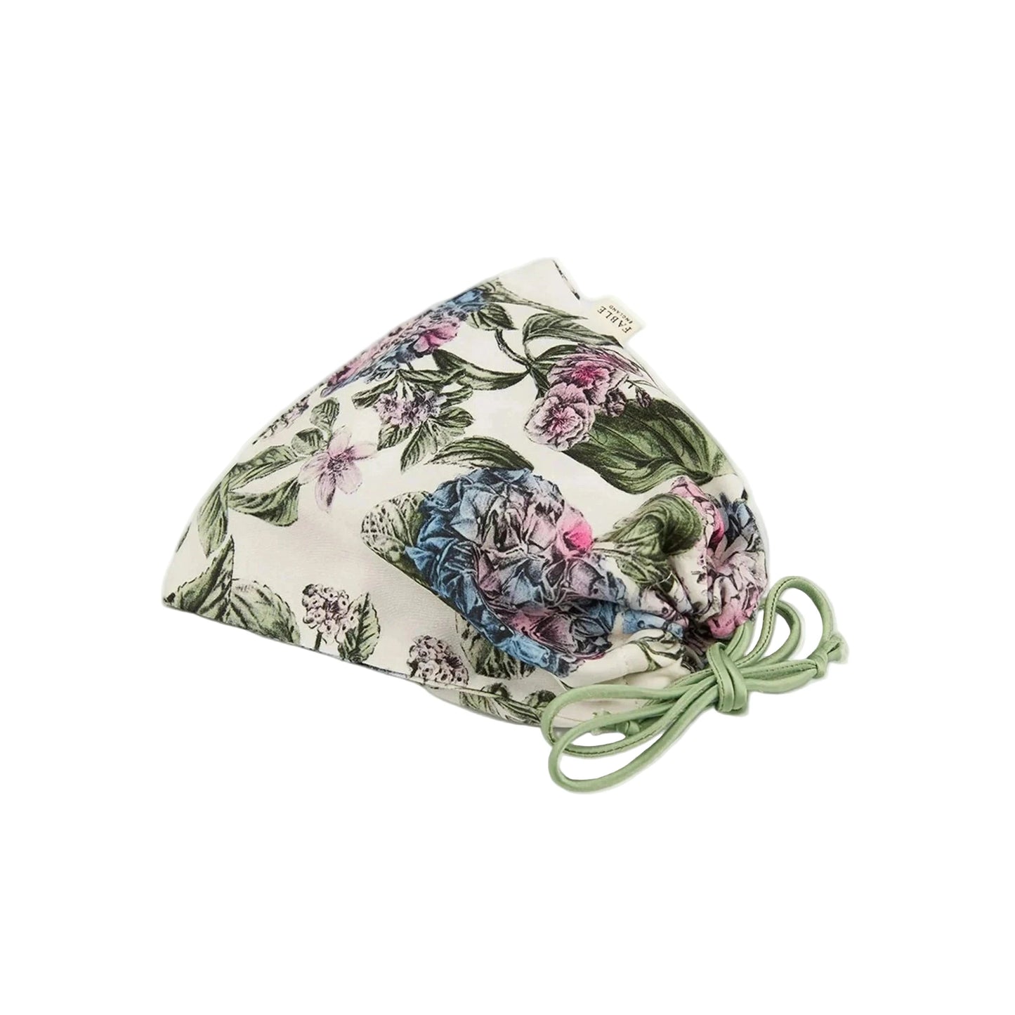 Zusammengelegte Schlafmaske mit botanischem Print in einem passenden Aufbewahrungsbeutel aus demselben Material, Beutel mit Kordelzug in Dunkelblau zum Zuziehen, Marken-Etikett sichtbar, zeigt die platzsparende Aufbewahrungslösung für unterwegs.
