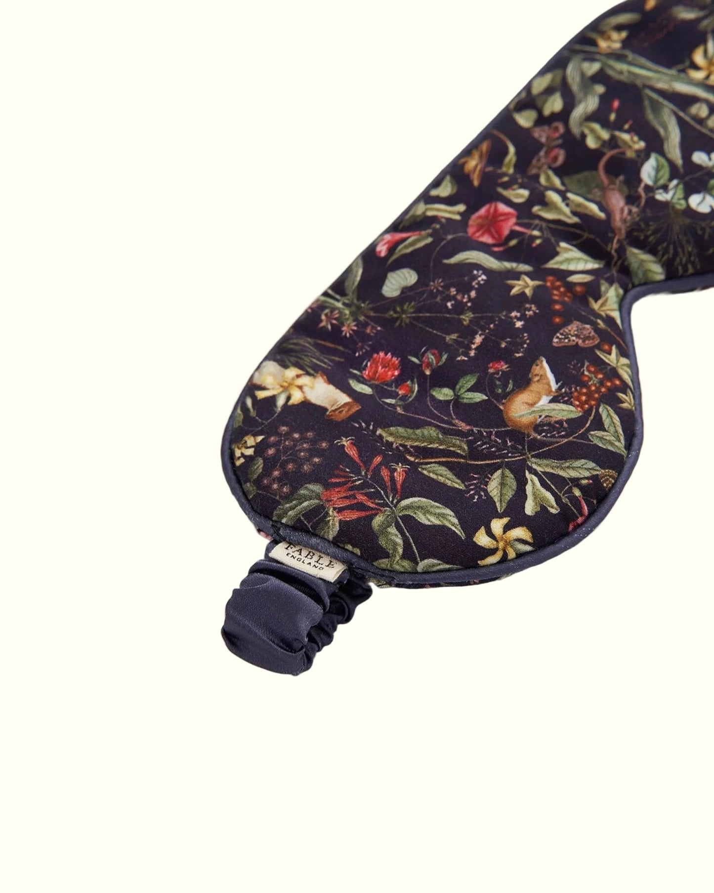 Schlafmaske aus Viskose mit kunstvollem botanischen Print: Wildblumen, Blätter, Beeren und Pflanzen in warmen Herbsttönen wie Rot, Orange, Gelb und Grün auf dunkelblauem bis schwarzem Untergrund; ergonomische Form mit weicher Polsterung und verstellbarem Satinband in Dunkelblau
