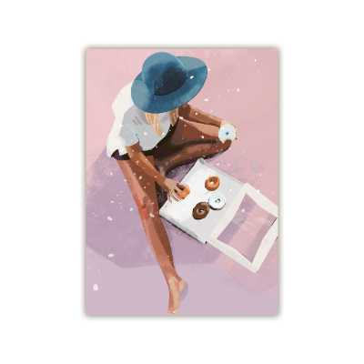 Frau mit blauem Hut sitzt im Sand, isst einen Donut und nimmt einen anderen Donut aus der Packung