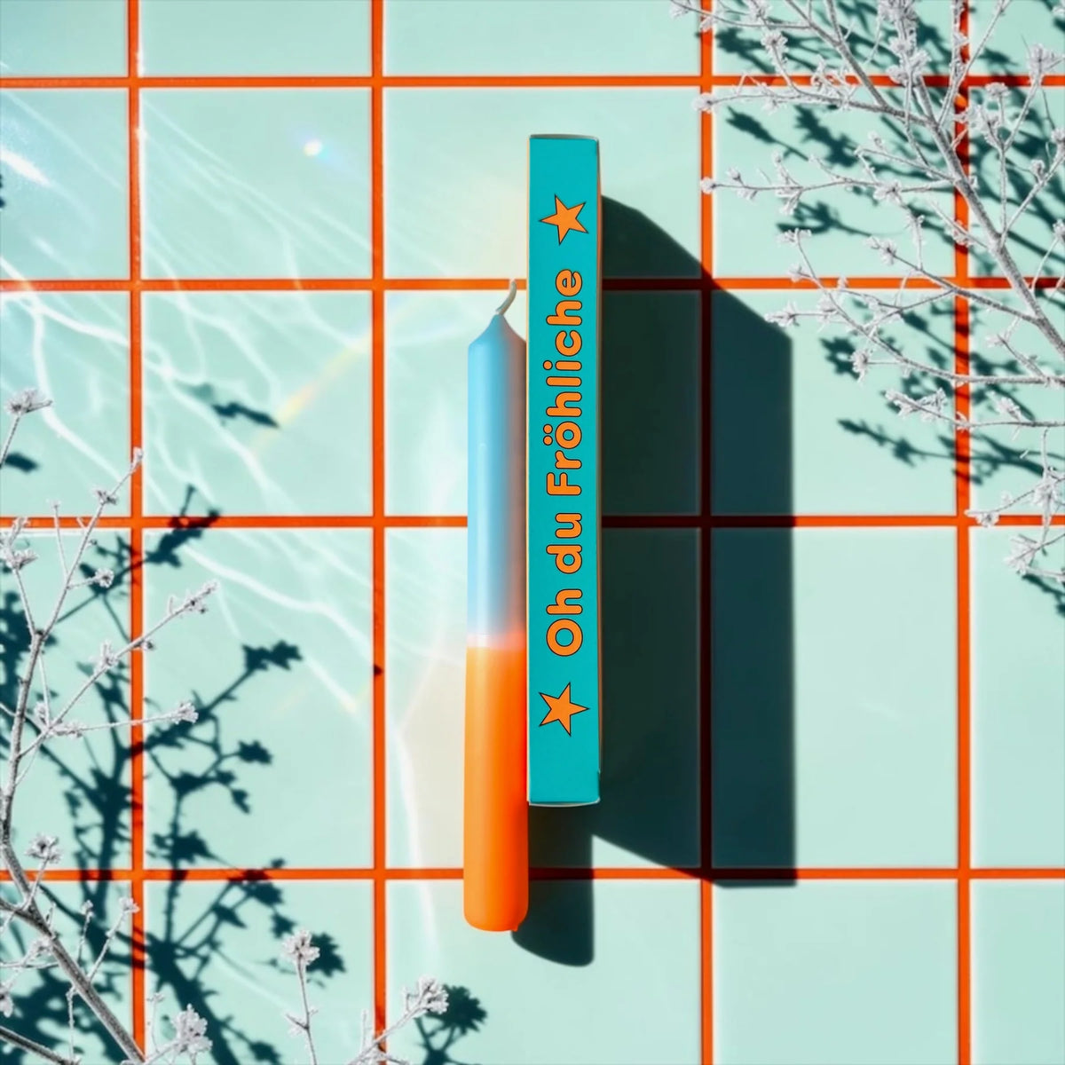 Eine weihnachtliche Dip-Dye-Stabkerze in Orange und Himmelblau von Pink Stories, neben der hellblauen Geschenkbox mit der Aufschrift „Oh du Fröhliche".