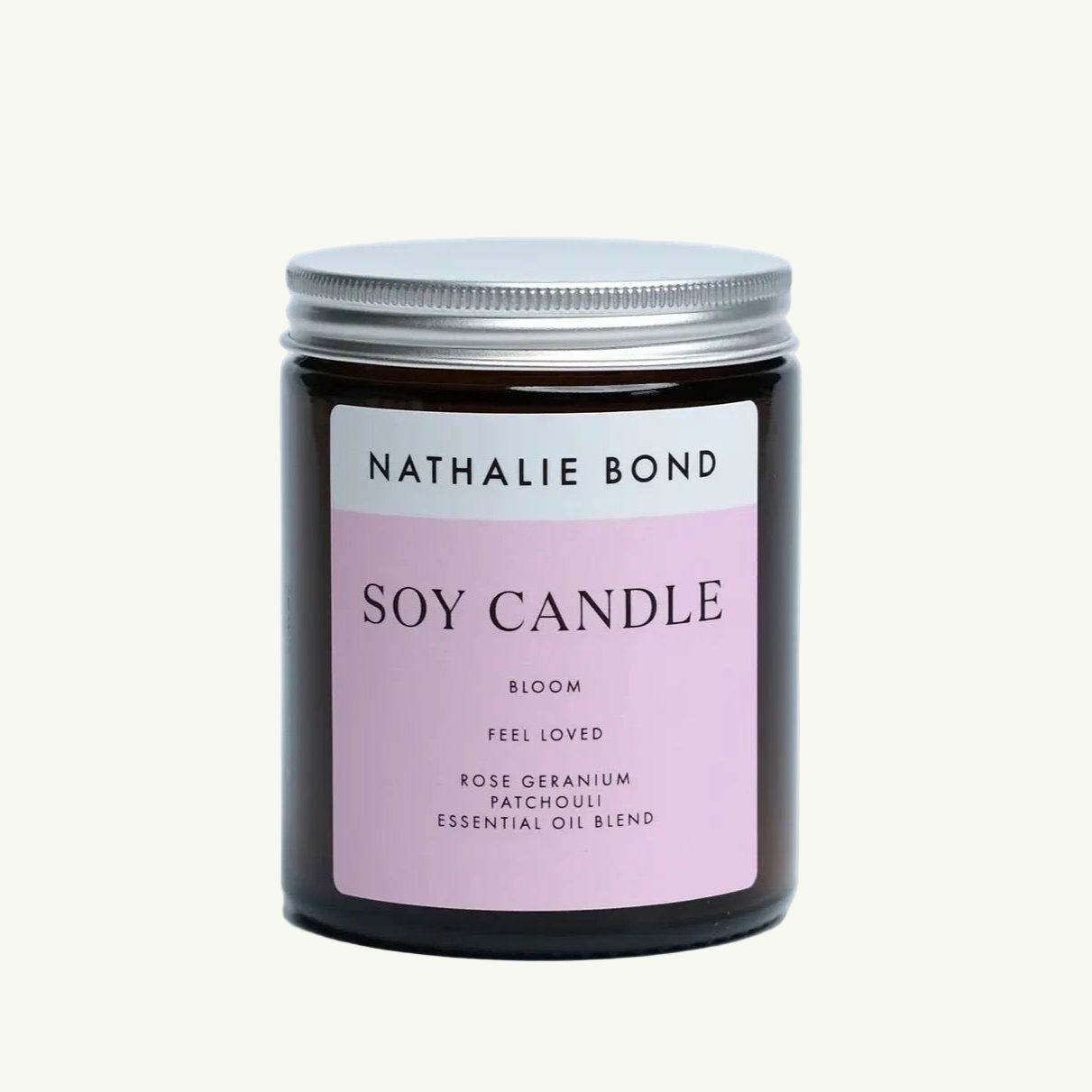 Duftkerze Nathalie Bond Braunes Glasglas mit silbernem Deckel, darauf ein rosa Etikett mit der Aufschrift 'NATHALIE BOND SOY CANDLE BLOOM FEEL LOVED ROSE GERANIUM PATCHOULI ESSENTIAL OIL BLEND'.