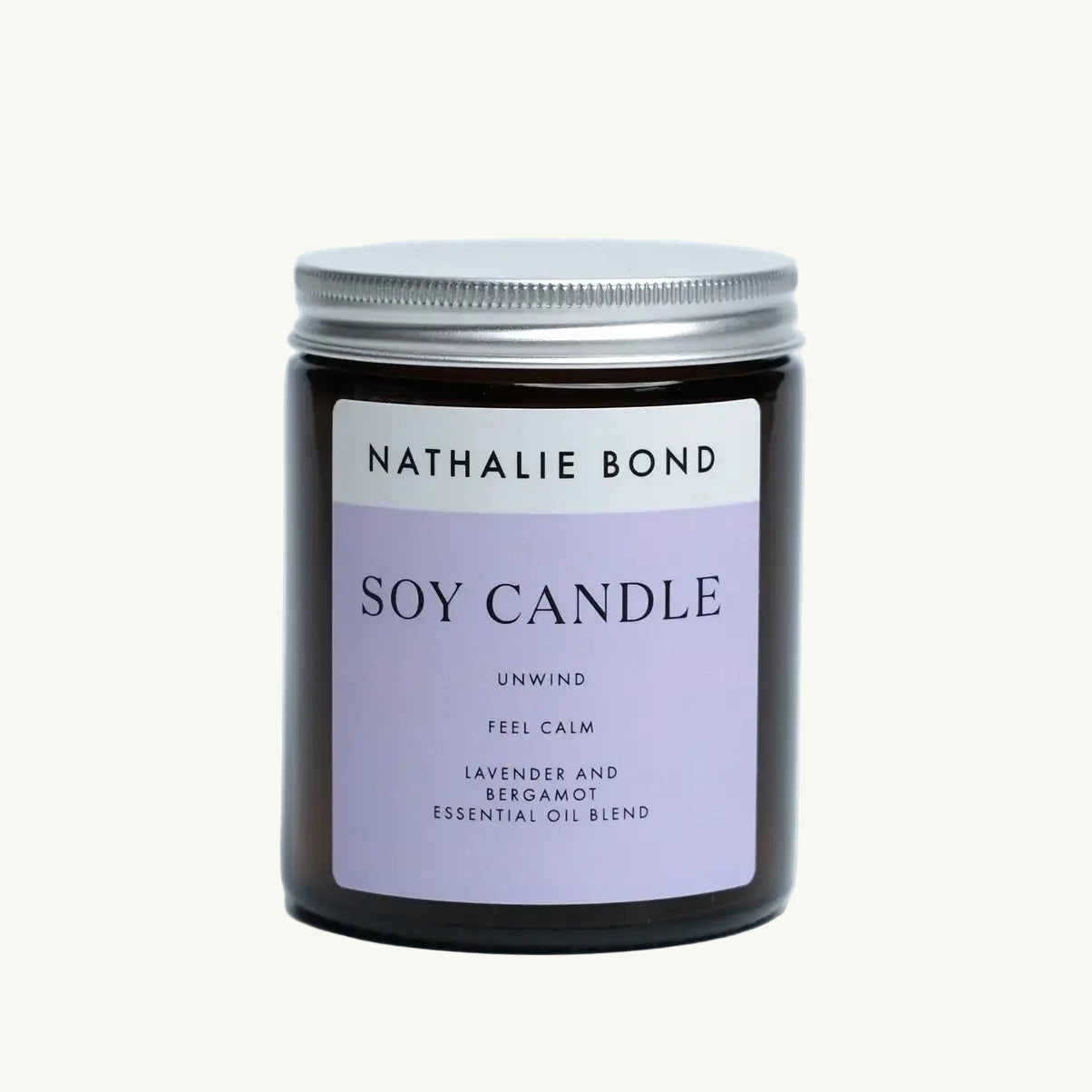Braunes Glasglas mit silbernem Deckel, darauf ein lila Etikett mit der Aufschrift 'NATHALIE BOND SOY CANDLE UNWIND FEEL CALM LAVENDER AND BERGAMOT ESSENTIAL OIL BLEND'.