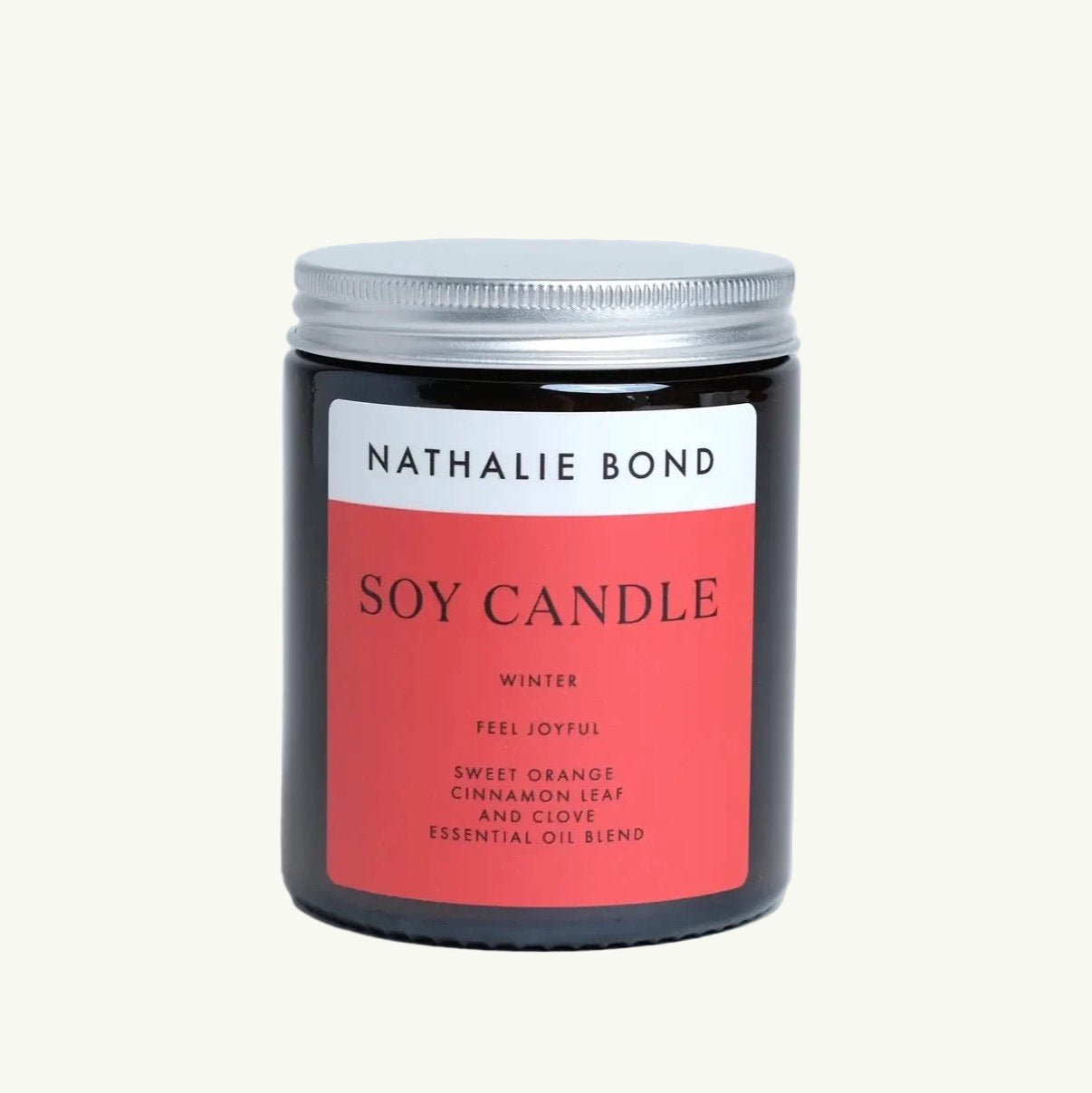 Braunes Glasglas mit silbernem Schraubdeckel, darauf ein rot-weißer Aufkleber mit schwarzer Schrift 'NATHALIE BOND SOY CANDLE WINTER FEEL JOYFUL