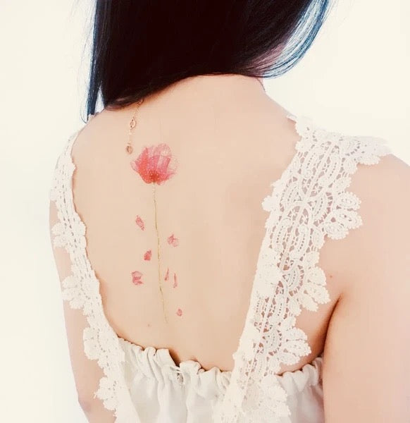 Frau mit schwarzem Haar zeigt Rücken mit rotem Mohnblumen-Tattoo und Spitzenkleid mit tiefem Rückenausschnitt