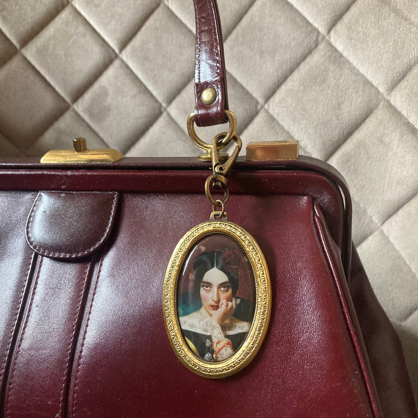 Weinrote Ledertasche mit goldfarbenem Rahmenanhänger in ovaler Form, der ein Frauenportrait zeigt