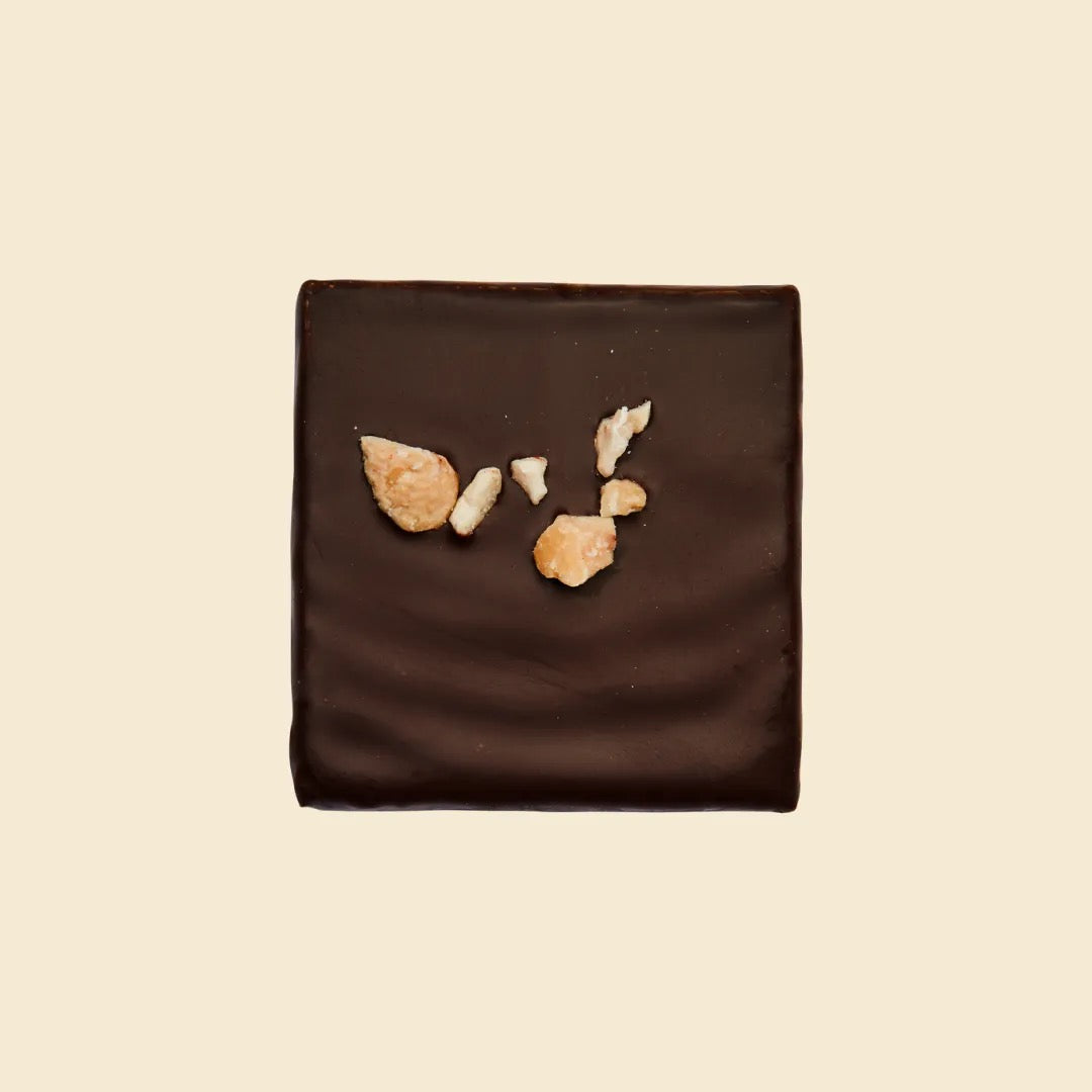 Nahaufnahme eines quadratischen dunklen Schokoladenriegels mit gehackten Cashewstücken als Topping.