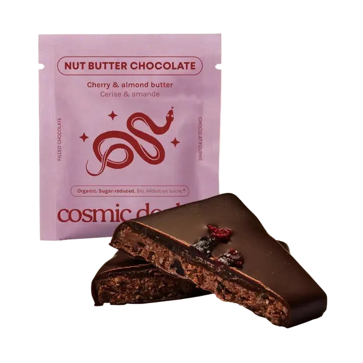 Eine halbierte Cosmic Dealer Cherry & Almond Butter Schokolade platziert vor ihrer hellvioletten Verpackung mit rotem Schlangen-Logo.
