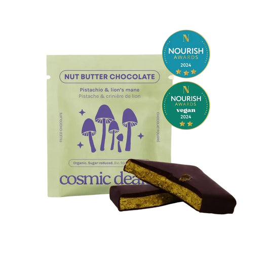 Eine Packung Cosmic Dealer Pistachio & Lion's Mane neben aufgeschnittenen Schokoladenriegeln, die die grüne Füllung zeigen.