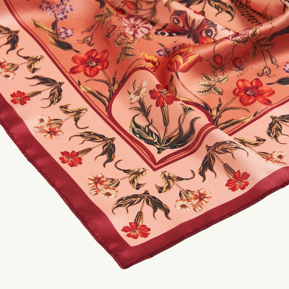 Quadratisches Tuch mit rotem Rand und floralem Muster in Rot, Blau und Beige, symmetrisch angeordnet.