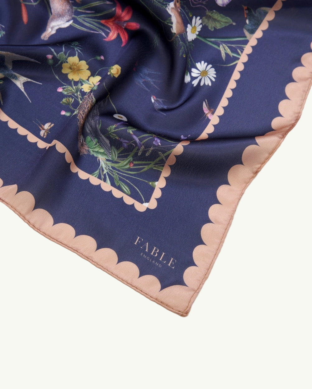 Quadratisches Tuch mit dunkelblauem Grund, floralem Muster in verschiedenen Farben und rosa gewelltem Rand.