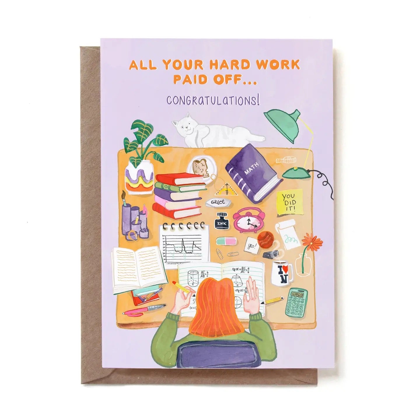 Eine illustrierte Glückwunschkarte zum bestandenen Abschluss mit der Aufschrift „ALL YOUR HARD WORK PAID OFF... CONGRATULATIONS!“. Das Motiv zeigt aus der Vogelperspektive eine Studentin mit roten Haaren am Schreibtisch, die in ihre Mathe-Hefte vertieft ist. Der Tisch ist voll mit Büchern, einem Mathebuch, einem Laptop, Notizen, einem Taschenrechner und einer Kaffeetasse. Eine weiße Katze liegt entspannt am oberen Schreibtischrand. Die Karte steckt in einem braunen Kraftpapier-Umschlag.