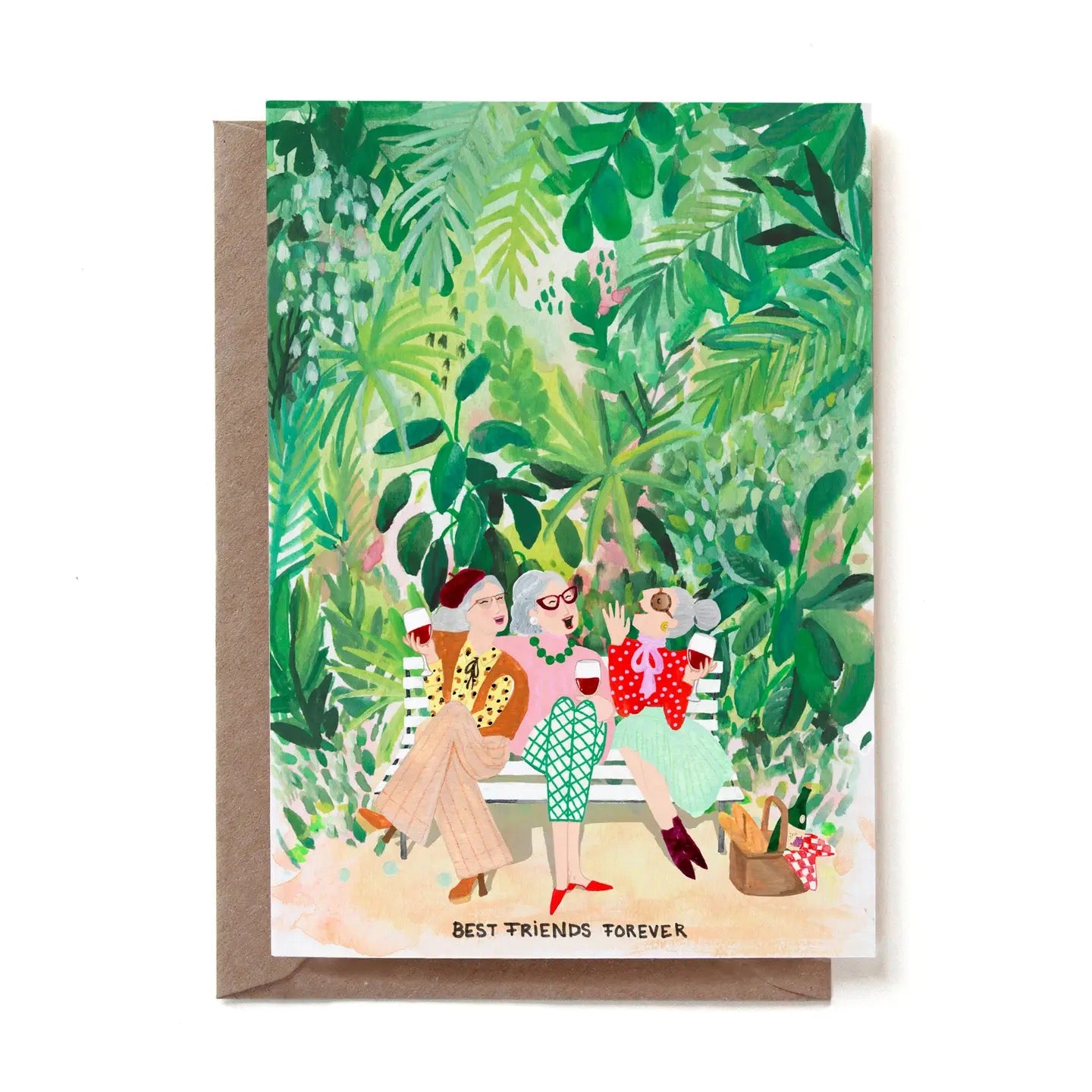 Eine illustrierte Freundschaftskarte mit der Aufschrift „BEST FRIENDS FOREVER“. Drei ältere, modisch gekleidete Frauen mit grauen Haaren sitzen glücklich plaudernd auf einer weißen Parkbank und stoßen mit Rotwein an. Sie befinden sich inmitten einer dichten, üppig grünen Kulisse aus Dschungelpflanzen und Palmenblättern. Neben der Bank steht ein Picknickkorb mit einem Baguette und einer Weinflasche. Die Karte steckt in einem braunen Kraftpapier-Umschlag.