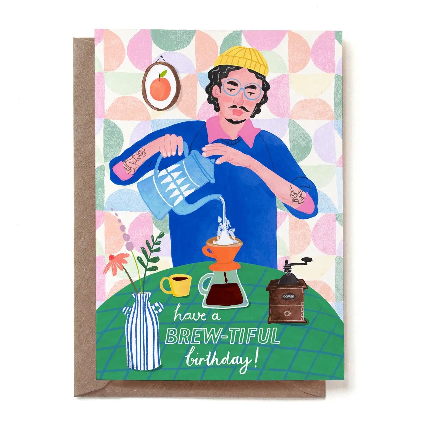 Eine illustrierte Geburtstagskarte für Kaffee-Liebhaber mit der Aufschrift „have a BREW-TIFUL birthday!“. Ein Mann mit Brille, gelber Strickmütze und Tätowierungen gießt heißes Wasser aus einer blau-weiß gemusterten Kanne in einen orangefarbenen Kaffeefilter. Auf dem grünen Tisch stehen zudem eine Kaffeemühle, eine gelbe Tasse und eine blau-weiß gestreifte Vase mit Blumen. Im Hintergrund ist ein pastellfarbenes Muster zu sehen. Die Karte steckt in einem braunen Kraftpapier-Umschlag.