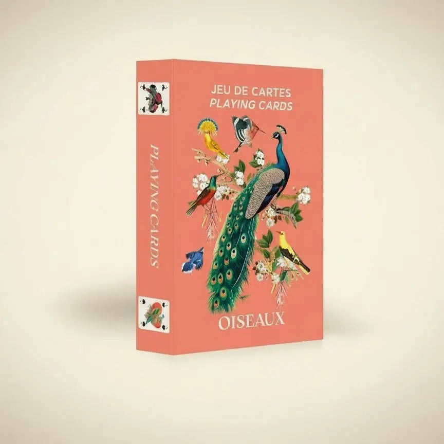 Eine geschlossene, hochkant stehende Produktbox des „Oiseaux“ Kartenspiels von Mon Petit Art. Die Box hat einen warmen, lachsfarbenen Hintergrund. Die Vorderseite zeigt eine detailreiche, klassische Illustration verschiedener Vögel, darunter ein prachtvoller Pfau auf einem blühenden Ast, ein Kolibri und ein gelber Pirol. Oben steht der Text „JEU DE CARTES / PLAYING CARDS“ und unten das Wort „OISEAUX“.