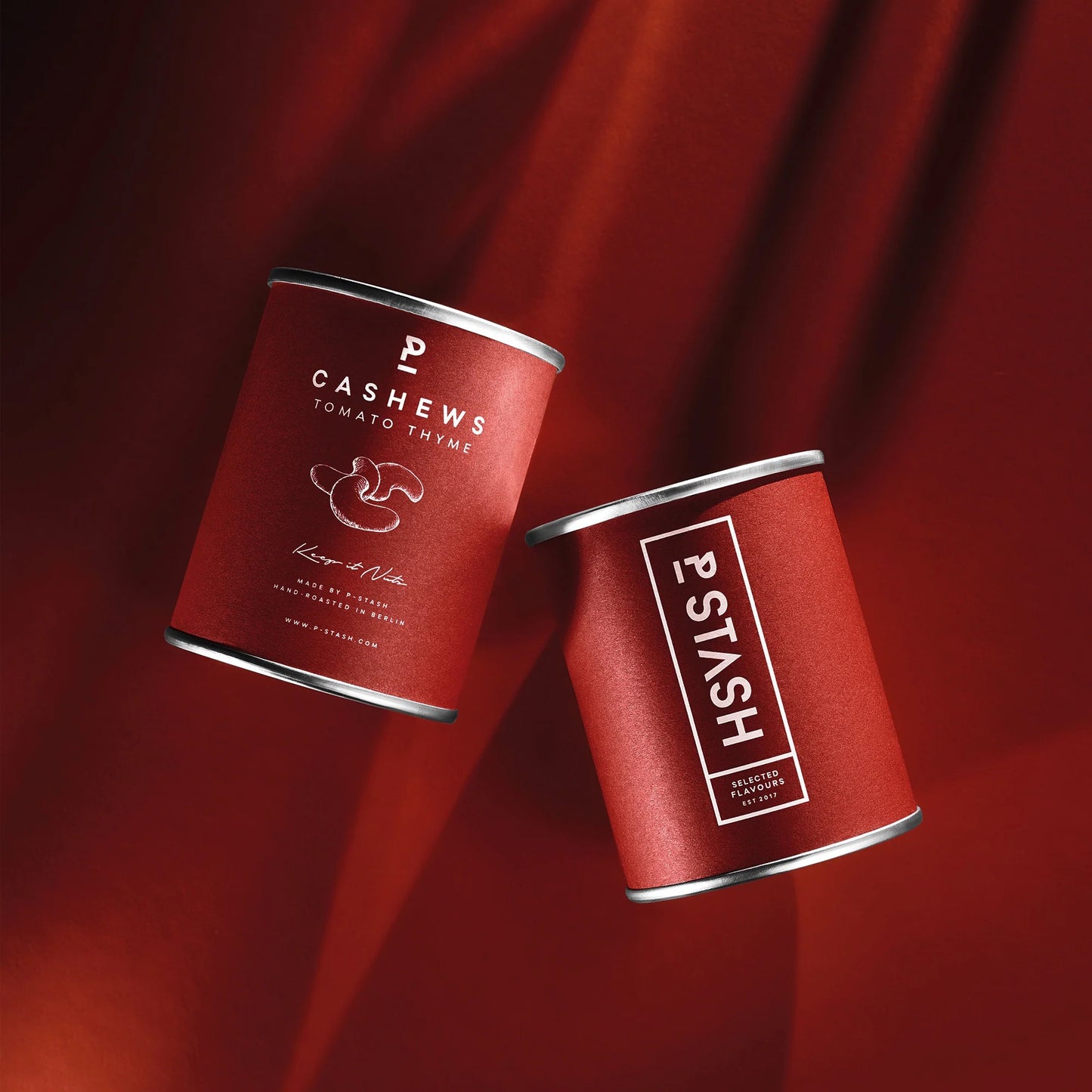 Eine Dose mit Aufschrift Cashews, Tomate und Thymian, daneben eine Dose mit Aufschrift P-STASH auf rotem Untergrund