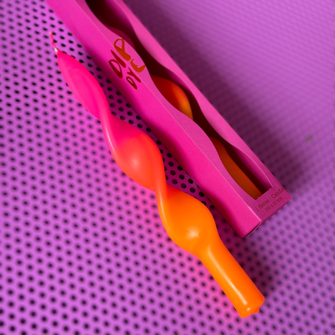 Zwei gedrehte Kerzen in Pink und Orange, eine in einer pinken Verpackung,