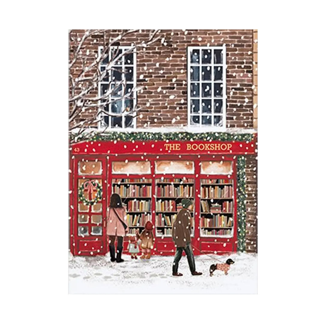 Illustrierte Winterszene vor einem roten Buchladen namens „THE BOOKSHOP“, während es schneit. Vor dem Schaufenster stehen eine Familie und eine Person, die einen Dackel im Pullover ausführt.