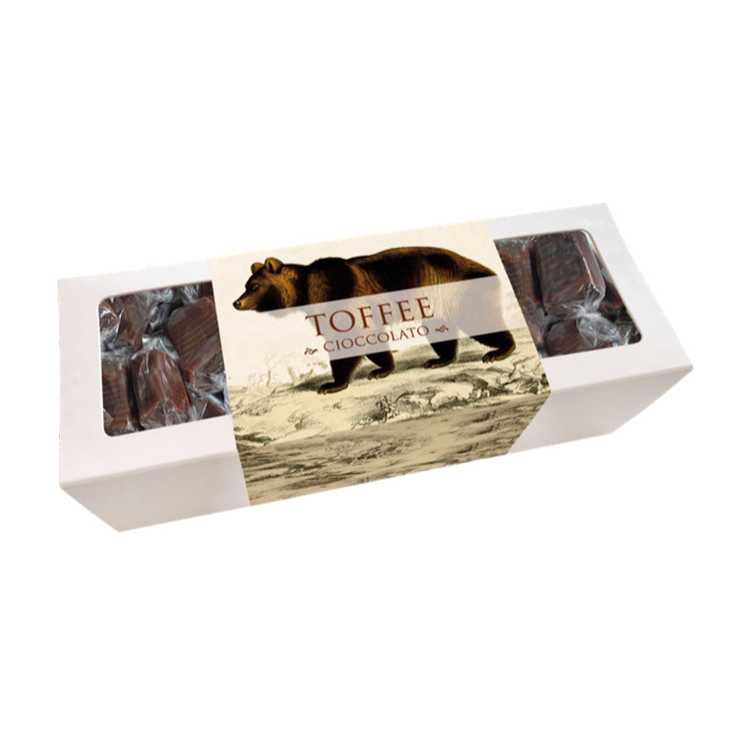 Weiße Schachtel mit durchsichtigen Fenstern, darin mehrere dunkle Toffee-Pralinen, Etikett mit braunem Bären und Schrift 'TOFFEE SCHOKOLADE'.