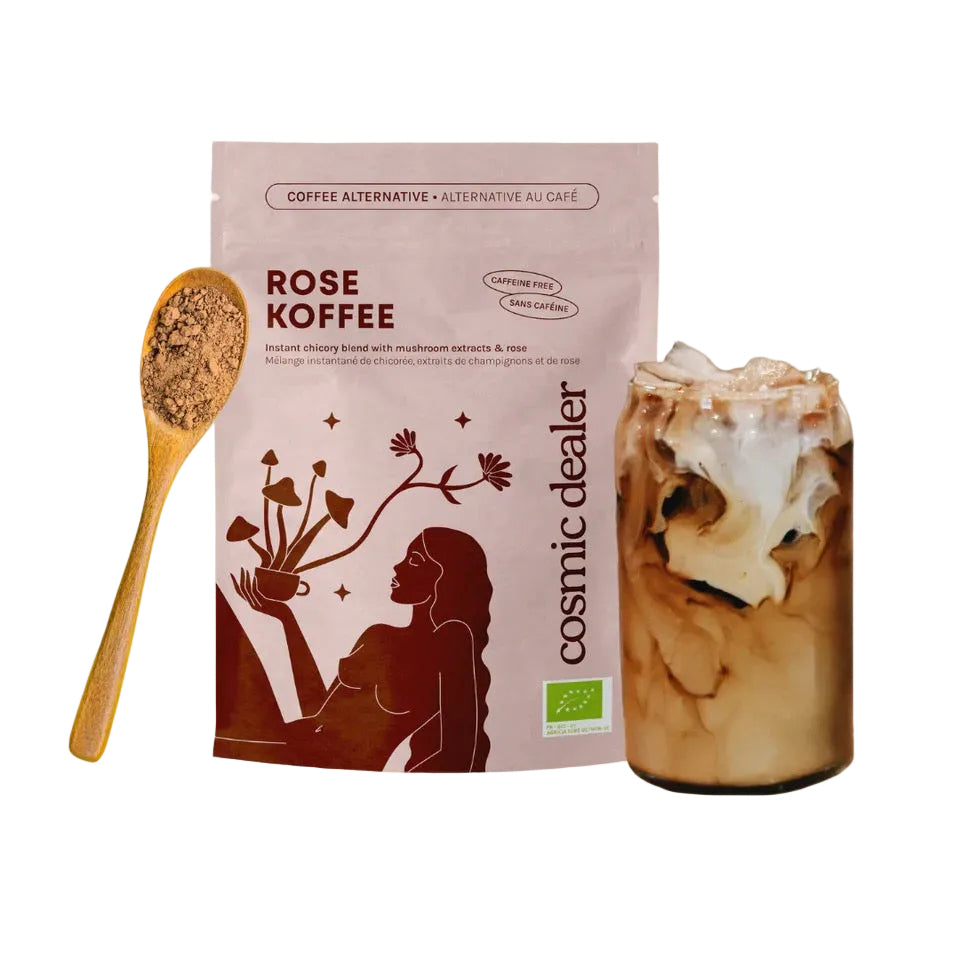 Zubereiteter Rose Koffee als Iced Latte mit Milchschaum neben der Originalverpackung und einem Holzlöffel mit dem dunklen Instant-Pulver.