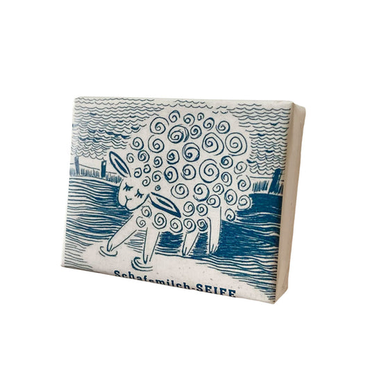 Schafemilch-Seife von 1000 und 1 Seife verpackt in weißem Papier mit einer blau gezeichneten Illustration eines Schafs im Wasser