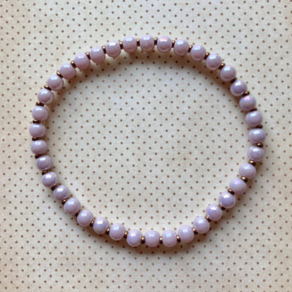 Einreihiges Perlenarmband in Lavendel,, kreisförmig angeordnet auf cremefarbenem Stoff mit Punkten.