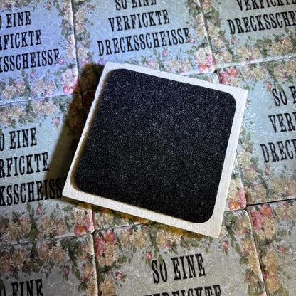 Quadratische Fliese von hinten mit filz, im Hintergrund fliesen mit Blumenmuster und dem Text 'SO EINE VERFICKTE DRECKSSCHEISSE' in Großbuchstaben