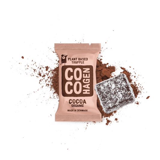 CocoHagen pflanzlicher Bio-Kakaotrüffel in rosafarbener Verpackung mit Kakaopulver und Kokosnuss auf weißem Hintergrund, unverpackter dunkler Schokoladentrüffel in Kokosnuss gerollt neben der Verpackung, hergestellt in Dänemark