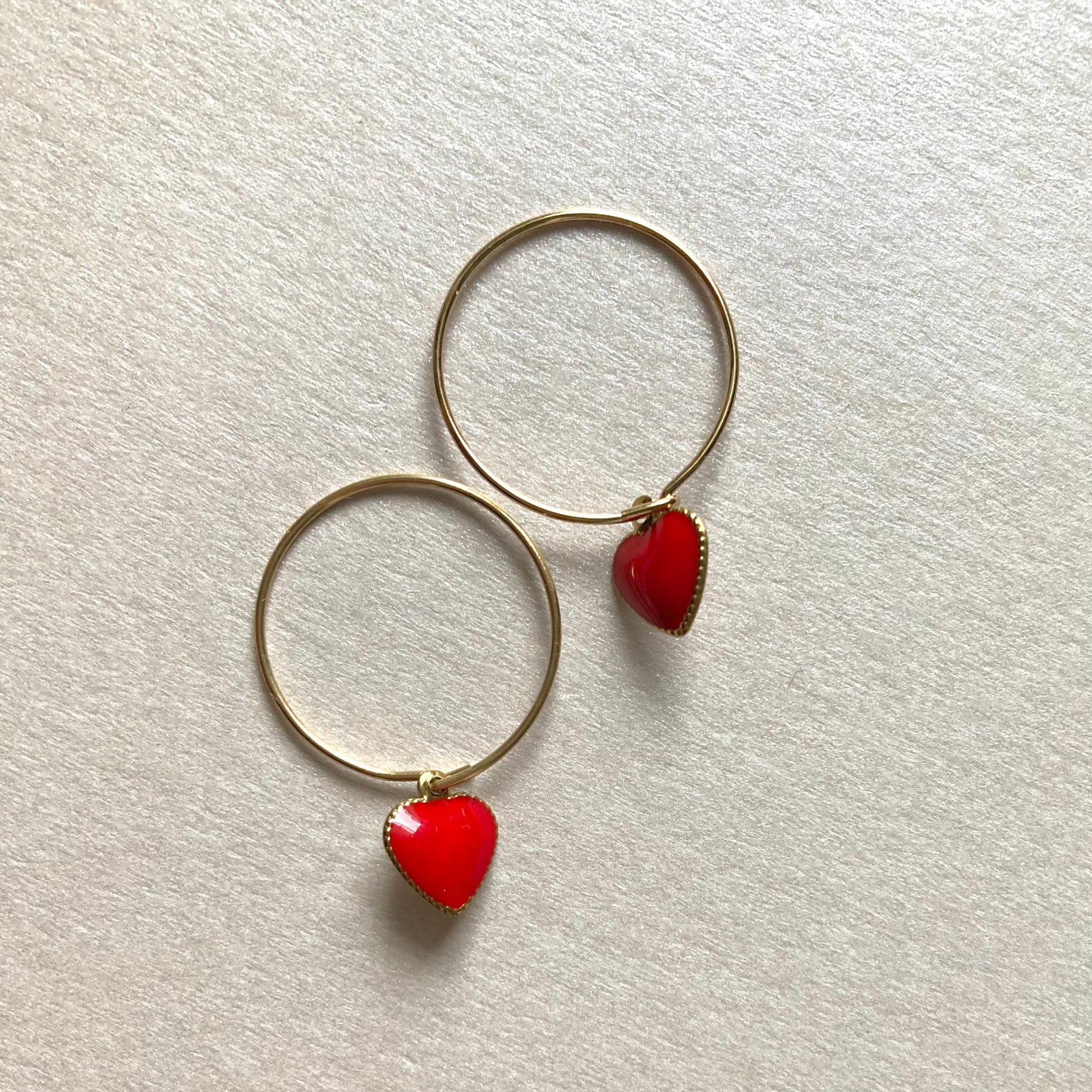 1 Paar goldfarbene Creolen mit herzförmigen Anhängern in Rot.