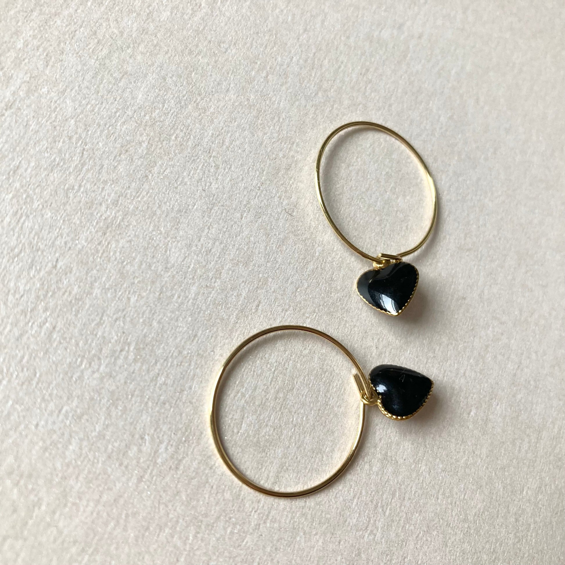 1 Paar goldfarbene Creolen mit herzförmigen Anhängern in Schwarz.