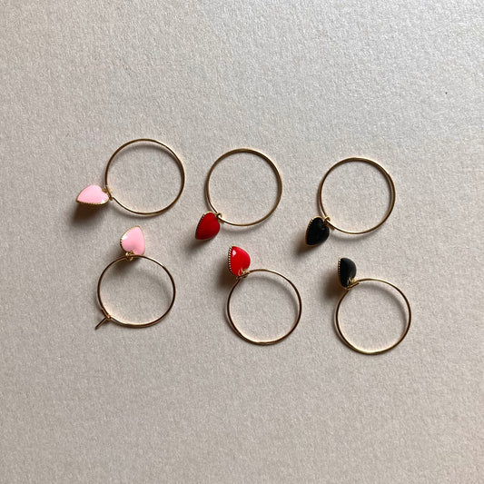 3 Paar goldfarbene Creolen mit herzförmigen Anhängern in Schwarz, Rot und Rosa, auf hellem Untergrund.