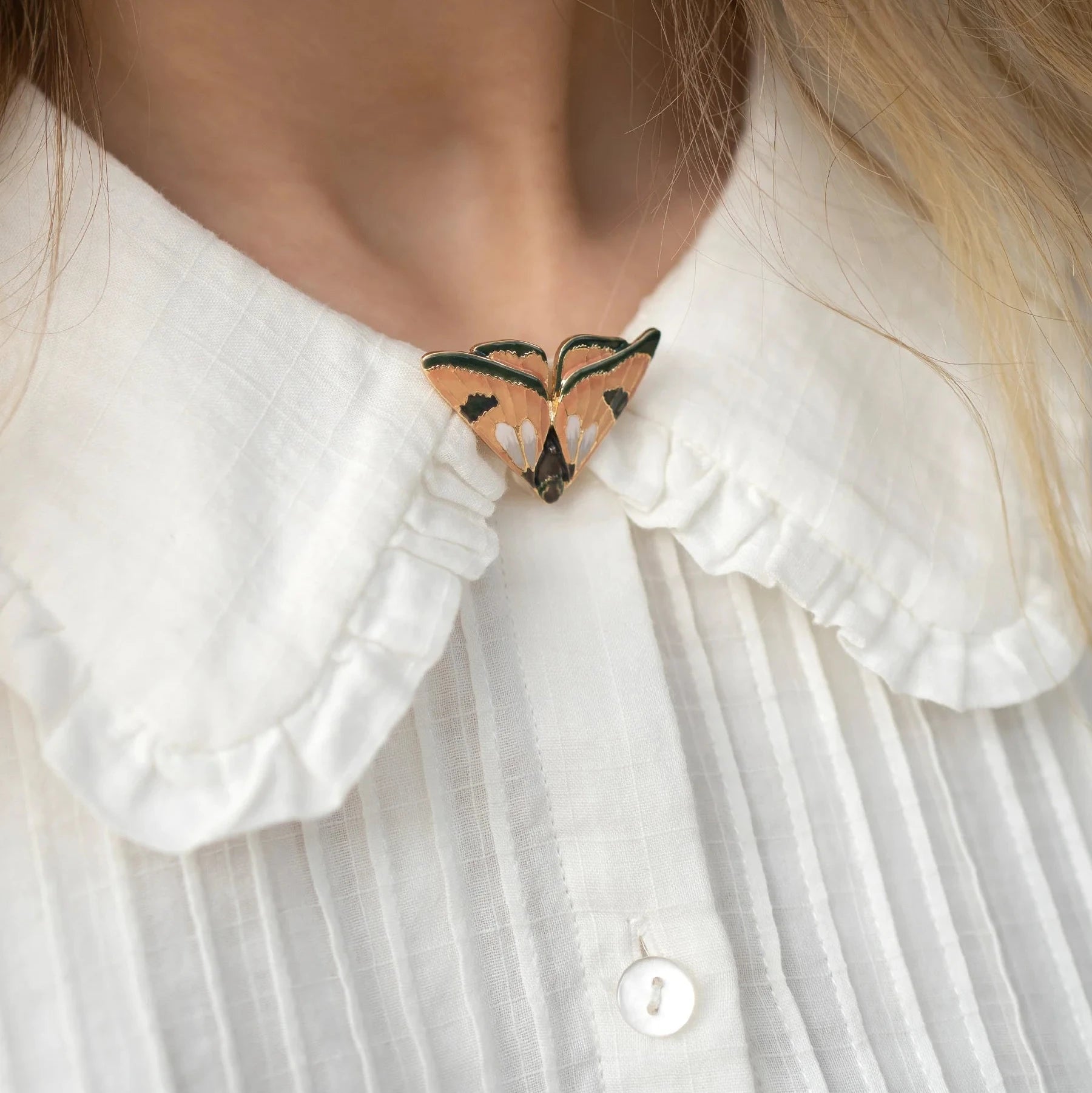 Nahaufnahme eines weißen Hemdkragens mit Rüschen, der mit einer Schmetterlingsbrosche in Beige und Schwarz geschlossen ist.