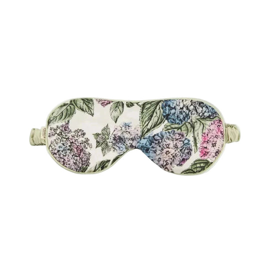 Luxuriöse Schlafmaske mit botanischem Hortensien-Design: große Blütendolden in zartem Rosa, Blau, Flieder und Grautönen mit grünen Blättern auf cremefarbenem Hintergrund, hellgrüne Satinpaspelierung und verstellbares elastisches Band in Mintgrün
