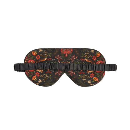 Schlafmaske mit künstlerischem Naturmotiv auf rotbraunem und schwarzem Untergrund: detaillierter Igel, Tagpfauenauge-Schmetterling, Wildblumen, Farnblätter und Beeren in warmen Herbstfarben wie Rostrot, Gelb, Grün und Orange, schwarzes Satinband mit Etikett, naturalistischer Vintage-Stil