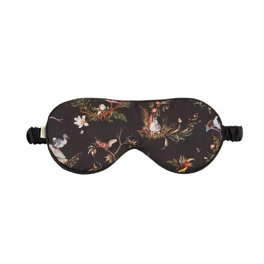 Schlafmaske mit künstlerischem Naturmotiv auf rotbraunem und schwarzem Untergrund: detaillierter Igel, Tagpfauenauge-Schmetterling, Wildblumen, Farnblätter und Beeren in warmen Herbstfarben wie Rostrot, Gelb, Grün und Orange, schwarzes Satinband mit Etikett, naturalistischer Vintage-Stil