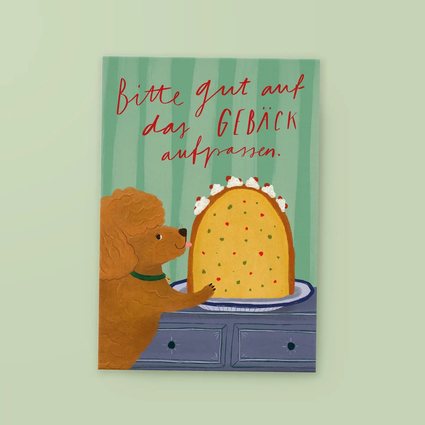 Brauner Pudel mit grünem Halsband neben großem Kuchen mit Zuckerguss auf blauem Tisch, Text 'Bitte gut auf das GEBÄCK aufpassen.' in roter Handschrift