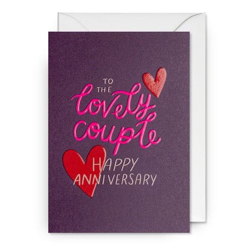 Lila Grußkarte mit zwei roten Herzen und dem Text 'TO THE lovely couple HAPPY ANNIVERSARY' in verschiedenen Schriftarten.
