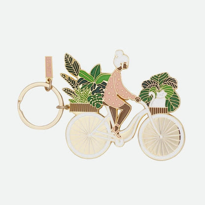 Schlüsselanhänger mit einer Person auf einem Fahrrad, umgeben von grünen Blättern, Details in Gold und Rosa