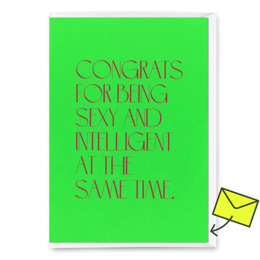 Eine Glückwunschkarte mit hellgrünem Hintergrund und dunklem Text mit der Aufschrift „Congrats for being sexy and intelligent“. In der oberen rechten Ecke befindet sich ein gelber „Deli Cards“-Aufkleber.