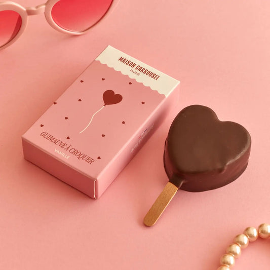 Herzförmiges Schokolade am Stiel neben einer rosa Verpackung mit der Aufschrift 'MAISON CARROUSEL PARIS' und 'GUIMAUVE À CROQUER VANILLE'.
