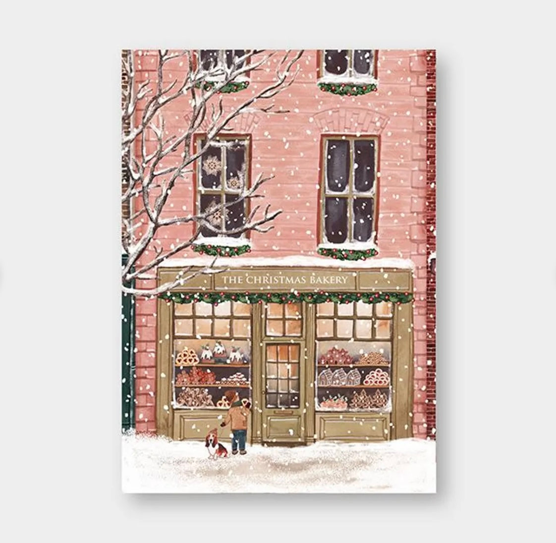 Schneefall vor einem zweistöckigen Backsteingebäude mit Bäckerei namens 'The Christmas Bakery', Schaufenster mit Weihnachtsgebäck, Person mit Hund davor.