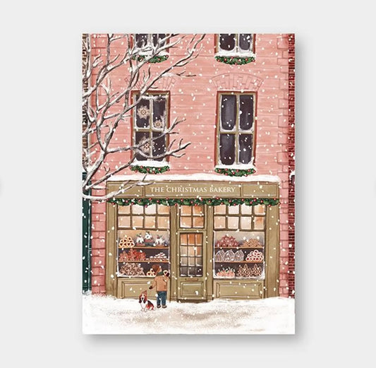 Schneefall vor einem zweistöckigen Backsteingebäude mit Bäckerei namens 'The Christmas Bakery', Schaufenster mit Weihnachtsgebäck, Person mit Hund davor.
