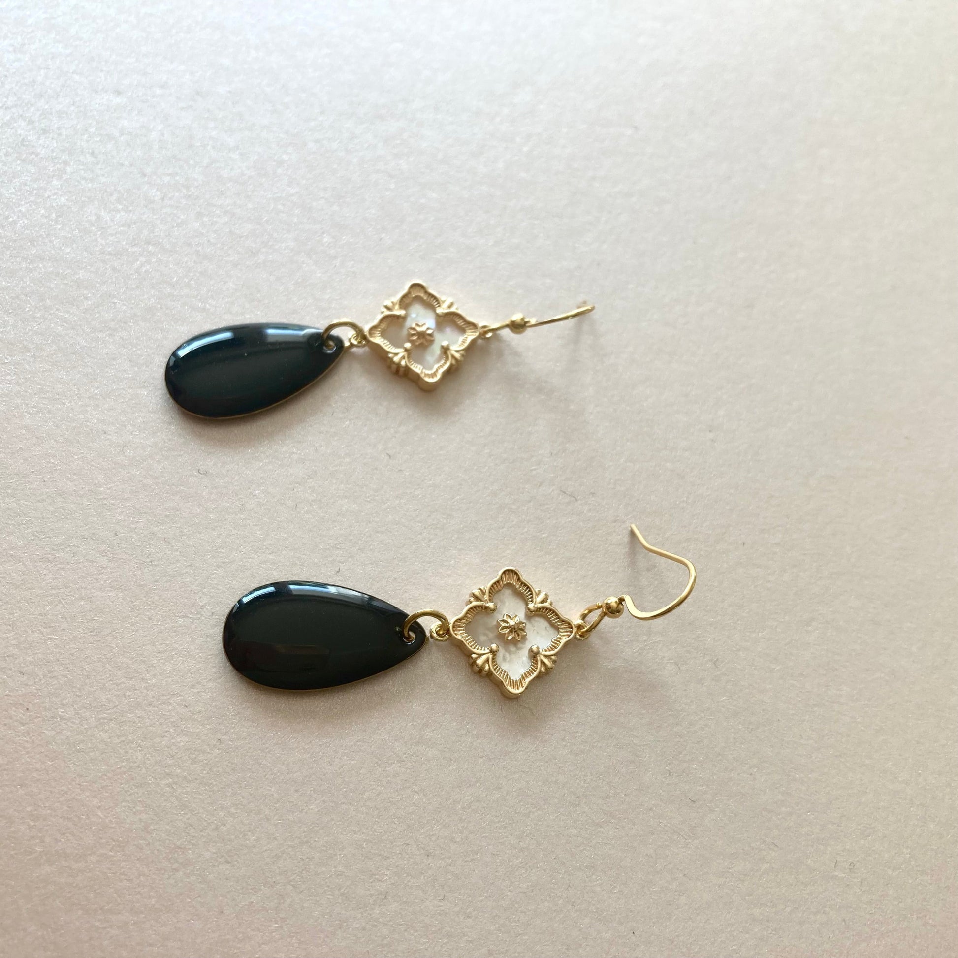 Ohrringe mit goldfarbenen Haken, goldfarbenen Perlmutt-Verbinder und schwarzen, tropfenförmigen Anhängern.